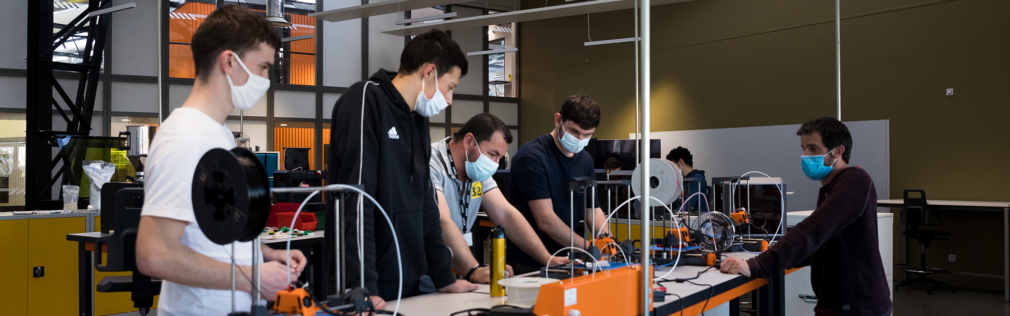 Apprenants et leur formateur travaillant sur des machines d'impression 3d dans le fablab